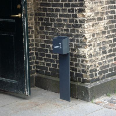 Et vægmonteret, minimalistisk askebæger i rustfrit stål fra Peoples ved siden af en kontorbygnings indgangsparti.